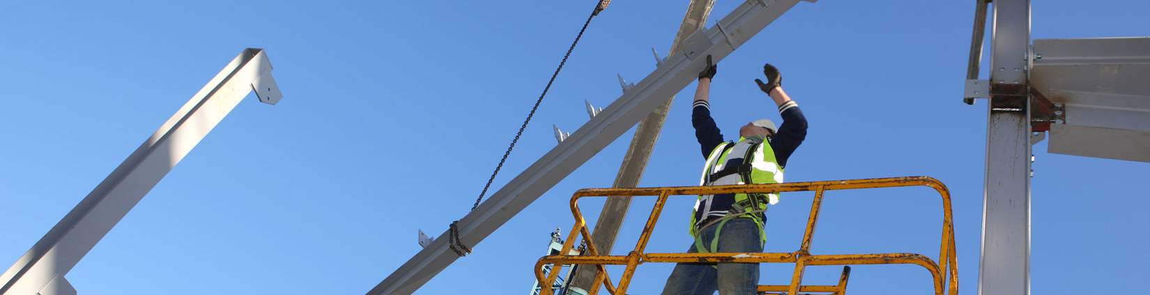 Image of a construction worker on a lift at a furnish and erect construction site This construction employee is trained in the construction of pre-engineered metal building such as Nucor Steel Building Systems.